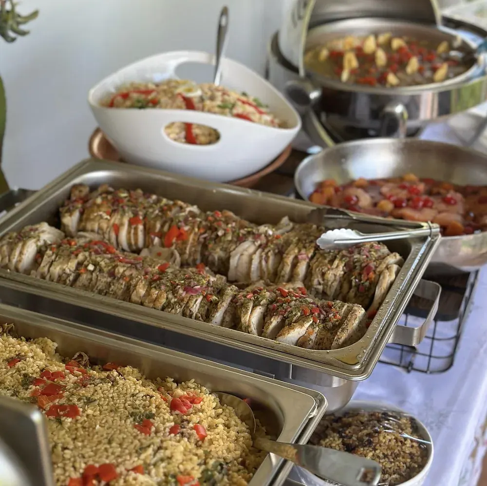 Buffet en chafing dishes de acero con pechuga de pollo en salsa de cilantro, arroz con vegetales y ensaladas