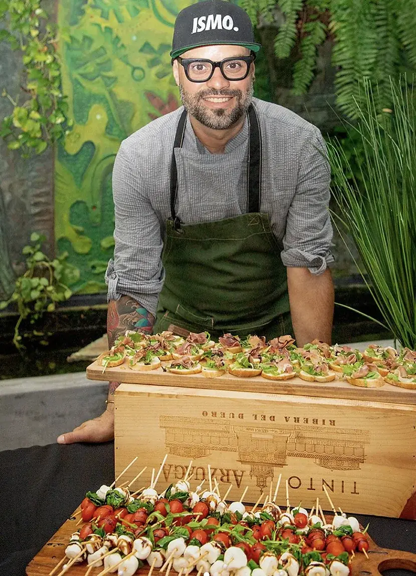 Miembro del equipo de SalteadosPR con delantal verde detrás de una tabla larga de crostini de prosciutto y brochetas de tomate y mozzarella