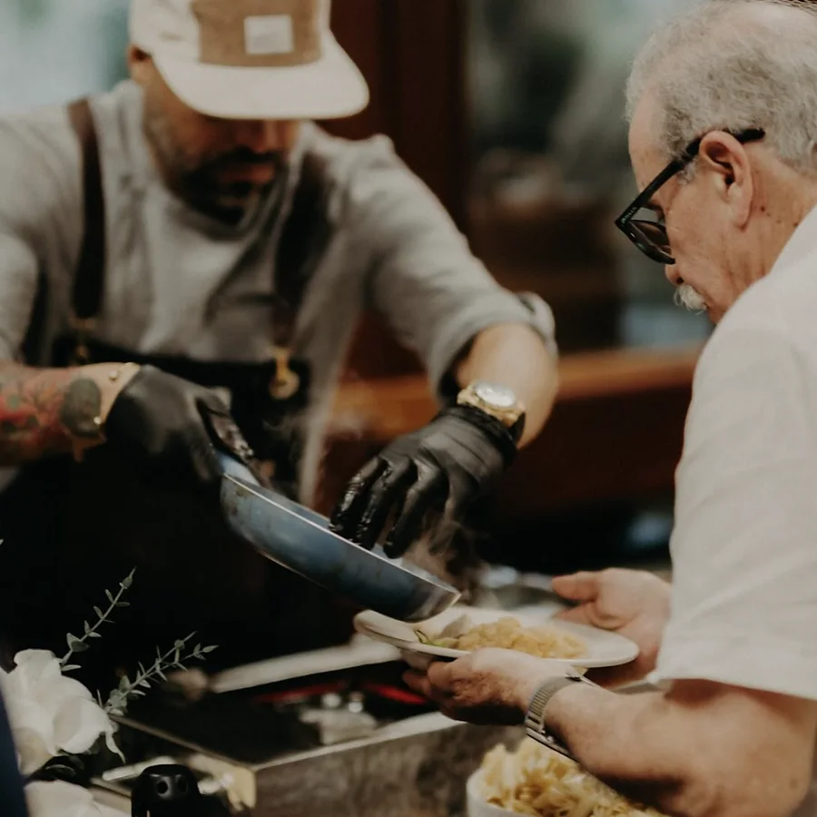 Chef de SalteadosPR sirviendo pasta humeante directamente del sartén al plato de un invitado durante un evento