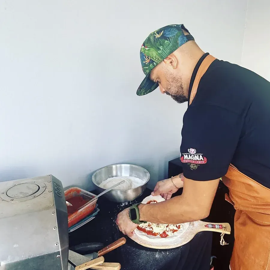 El chef de SalteadosPR armando una pizza a mano sobre la pala, junto al horno en la unidad móvil