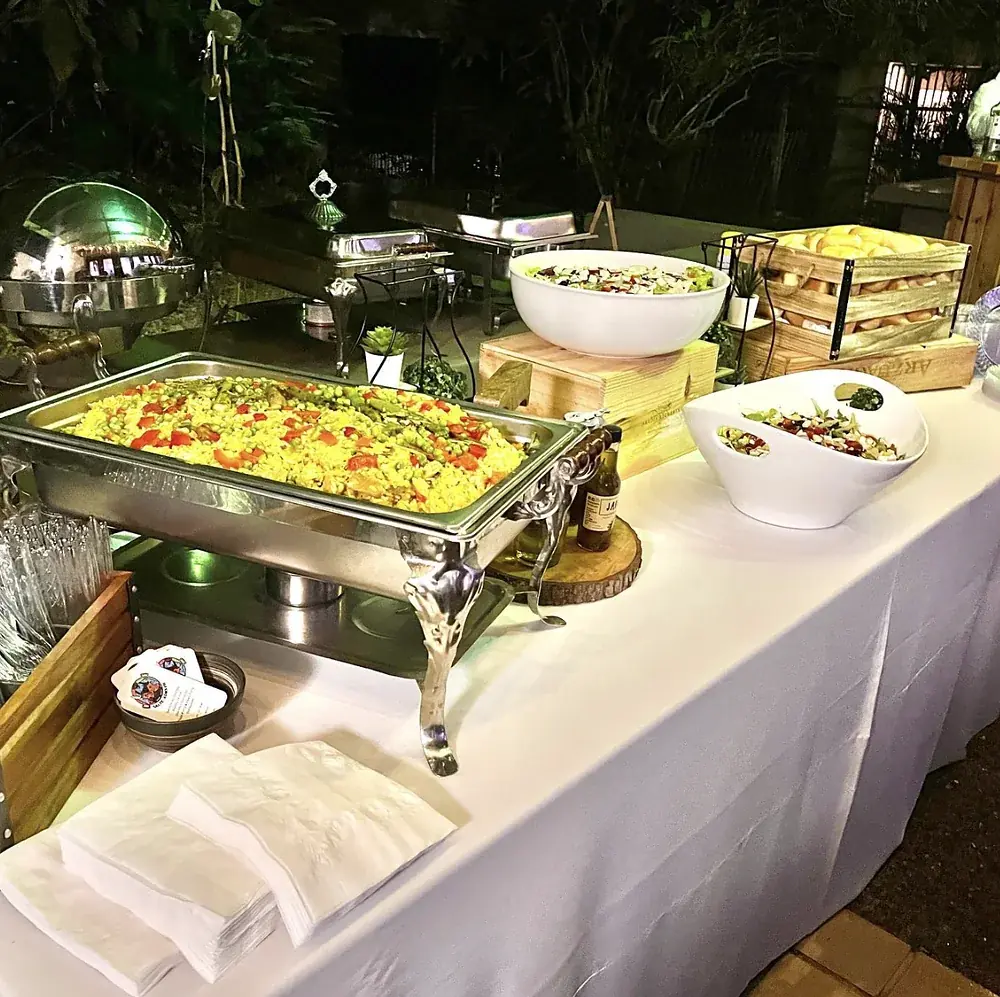 Paella servida en chafing dish de acero en un evento de noche al aire libre, con mantelería blanca y ensaladas