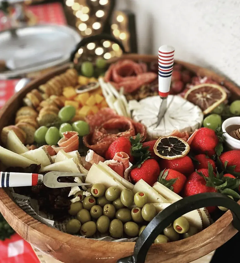 Tabla redonda de grazing con quesos, embutidos enrollados, aceitunas, fresas, uvas, cítricos deshidratados y miel